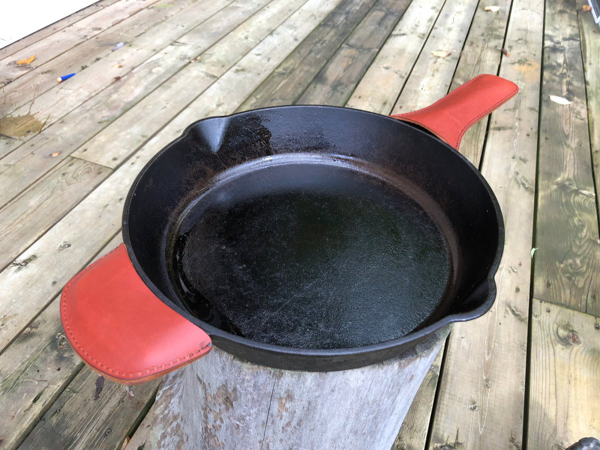 A black cast iron pan with a red leather handle cover fitted on the pan, displayed on a wooden surface.